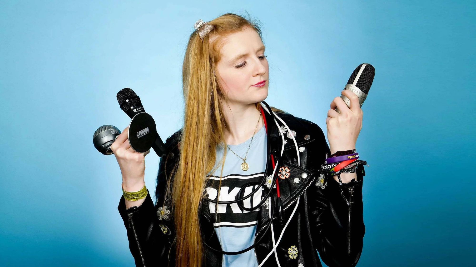 A woman holding three microphones. She's standing in front of a blue background.