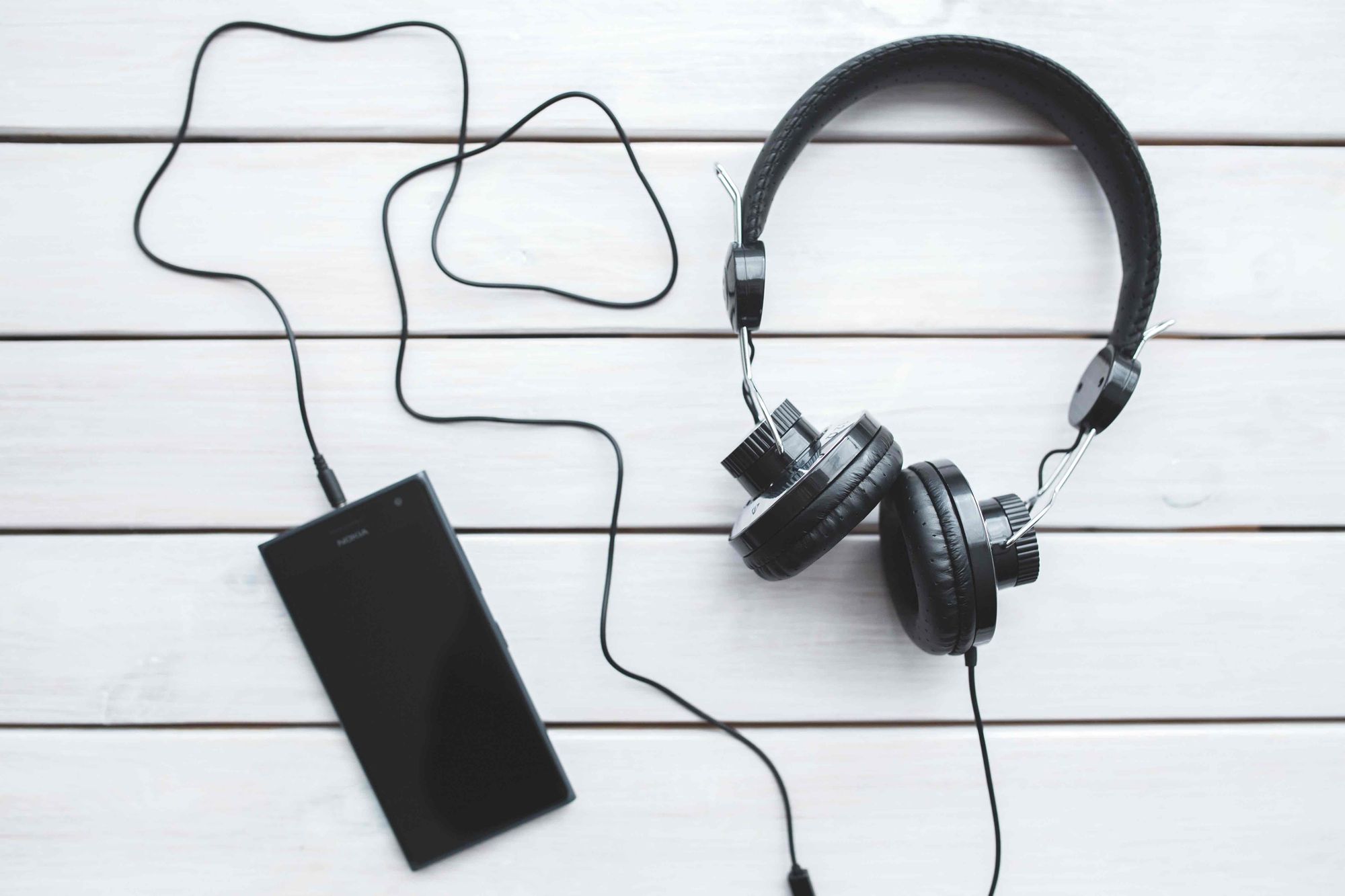 A pair of headphones plugged into a smartphone, on a table. 