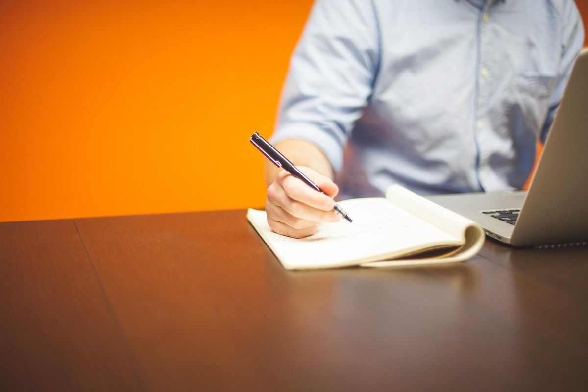 A man, at a desk, writing in a notebook.