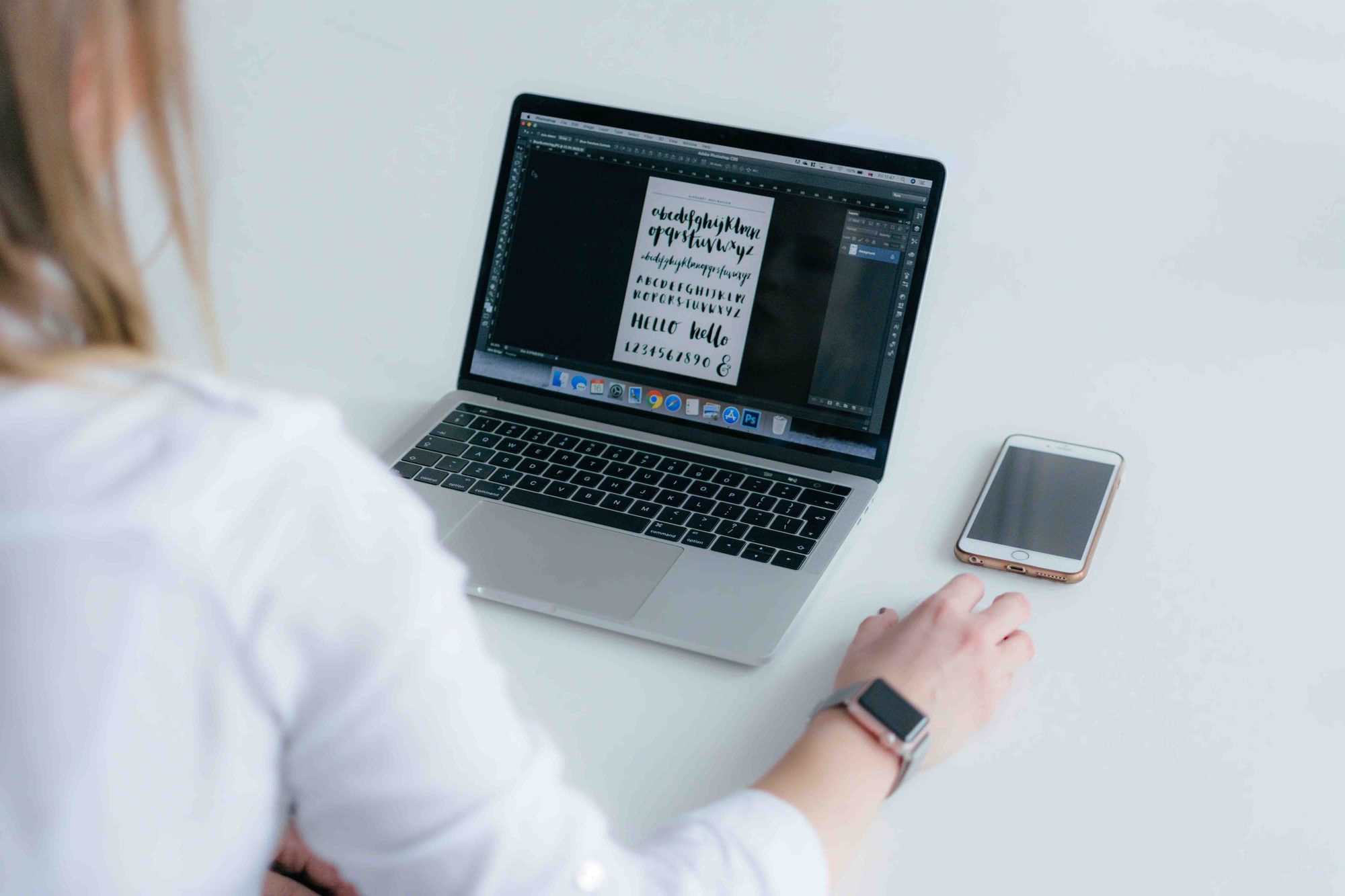 A woman sat at a computer, looking at various font types on the screen.