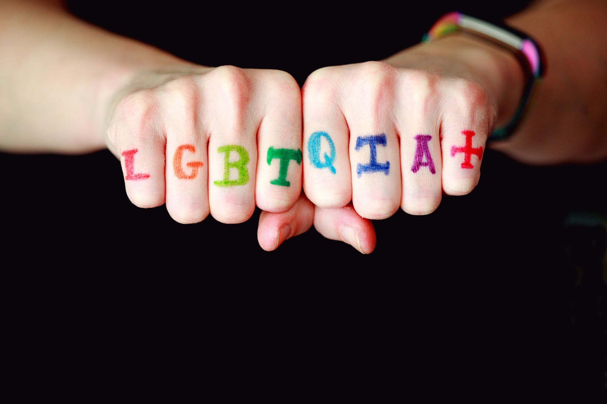 Two fists together with a letter on each knuckle. The letters spell out "LGBTQIA+"